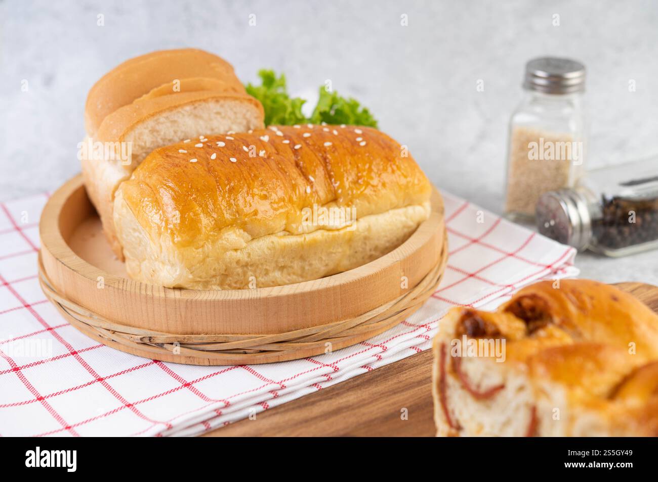 Pane in un vassoio di legno su un panno rosso e bianco con lattuga e mais. Foto Stock