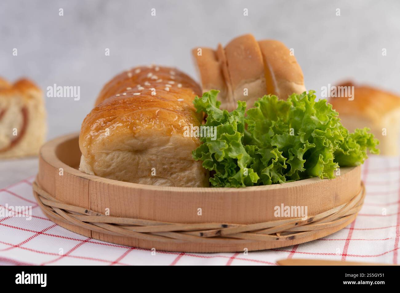 Pane in un vassoio di legno su un panno rosso e bianco con lattuga e mais. Foto Stock