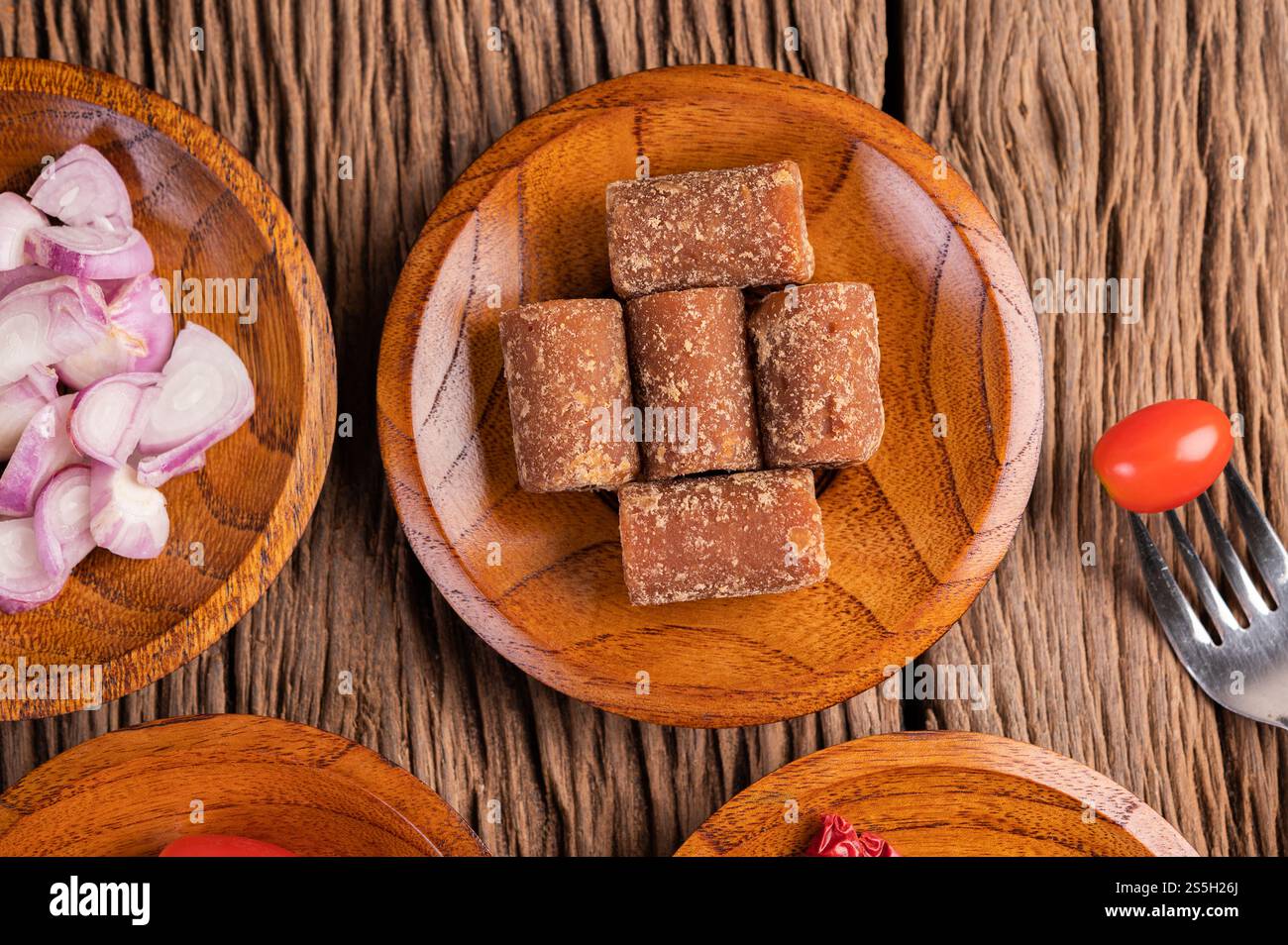Zucchero di palma e cipolle rosse su un piatto di legno con uno spiedino di pomodoro sul pavimento di legno. Foto Stock
