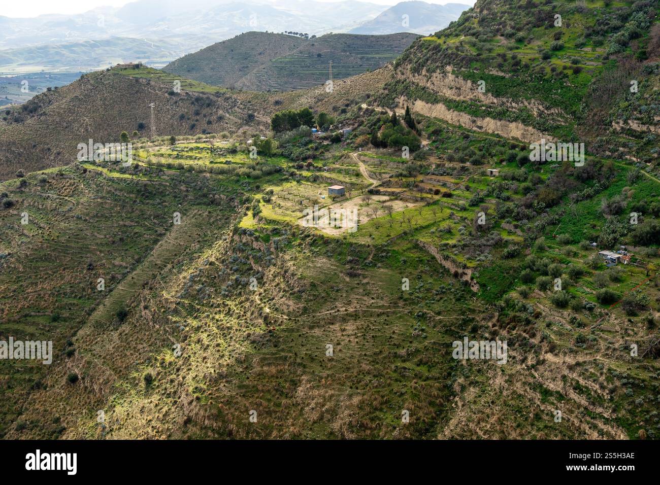 Paesaggio pittoresco della campagna siciliana: Colline ondulate, terrazze verdeggianti, fattorie rurali e oliveti sotto la luce soffusa del sole: Autentica Medite Foto Stock