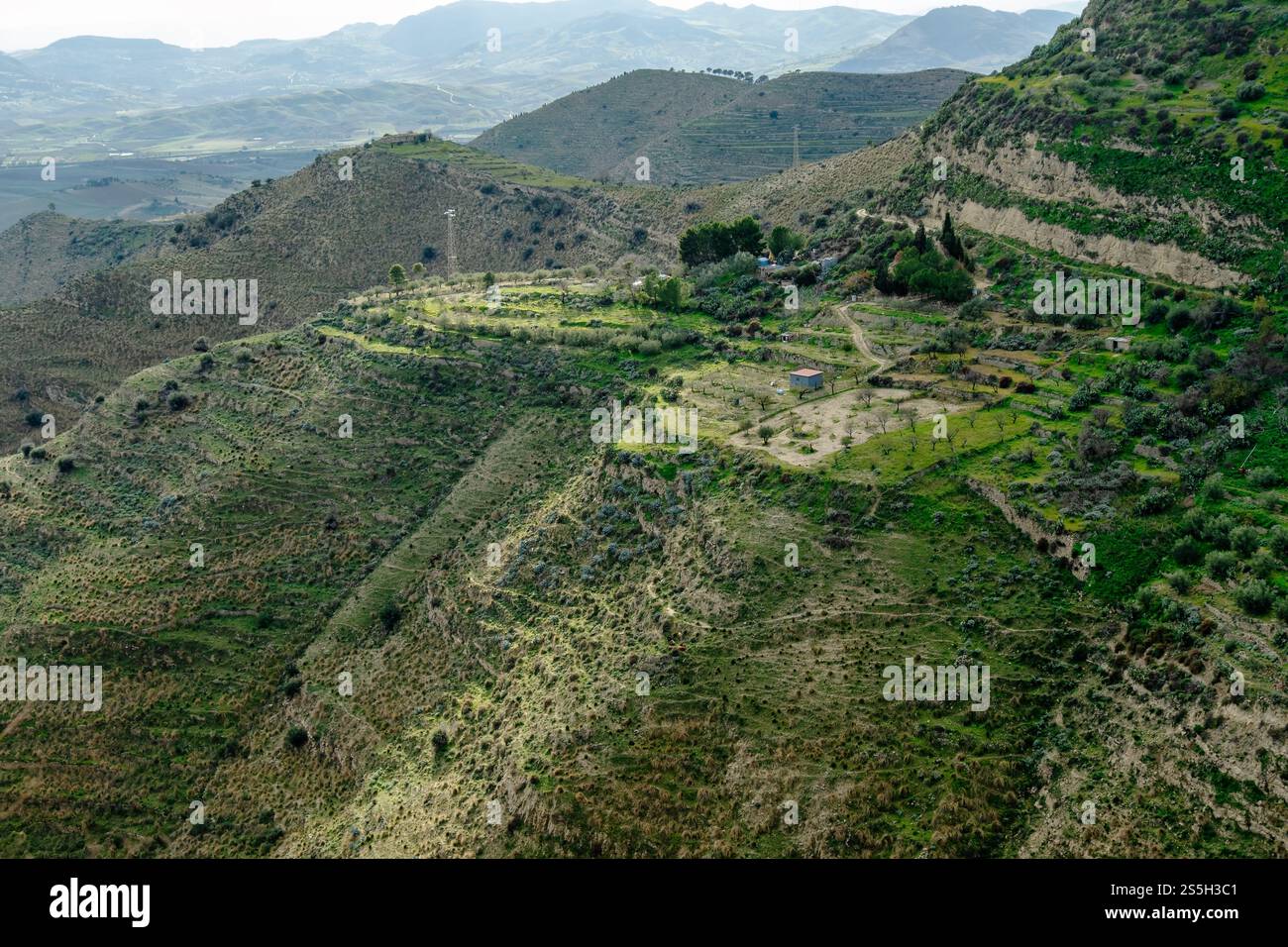 Paesaggio pittoresco della campagna siciliana: Colline ondulate, terrazze verdeggianti, fattorie rurali e oliveti sotto la luce soffusa del sole: Autentica Medite Foto Stock