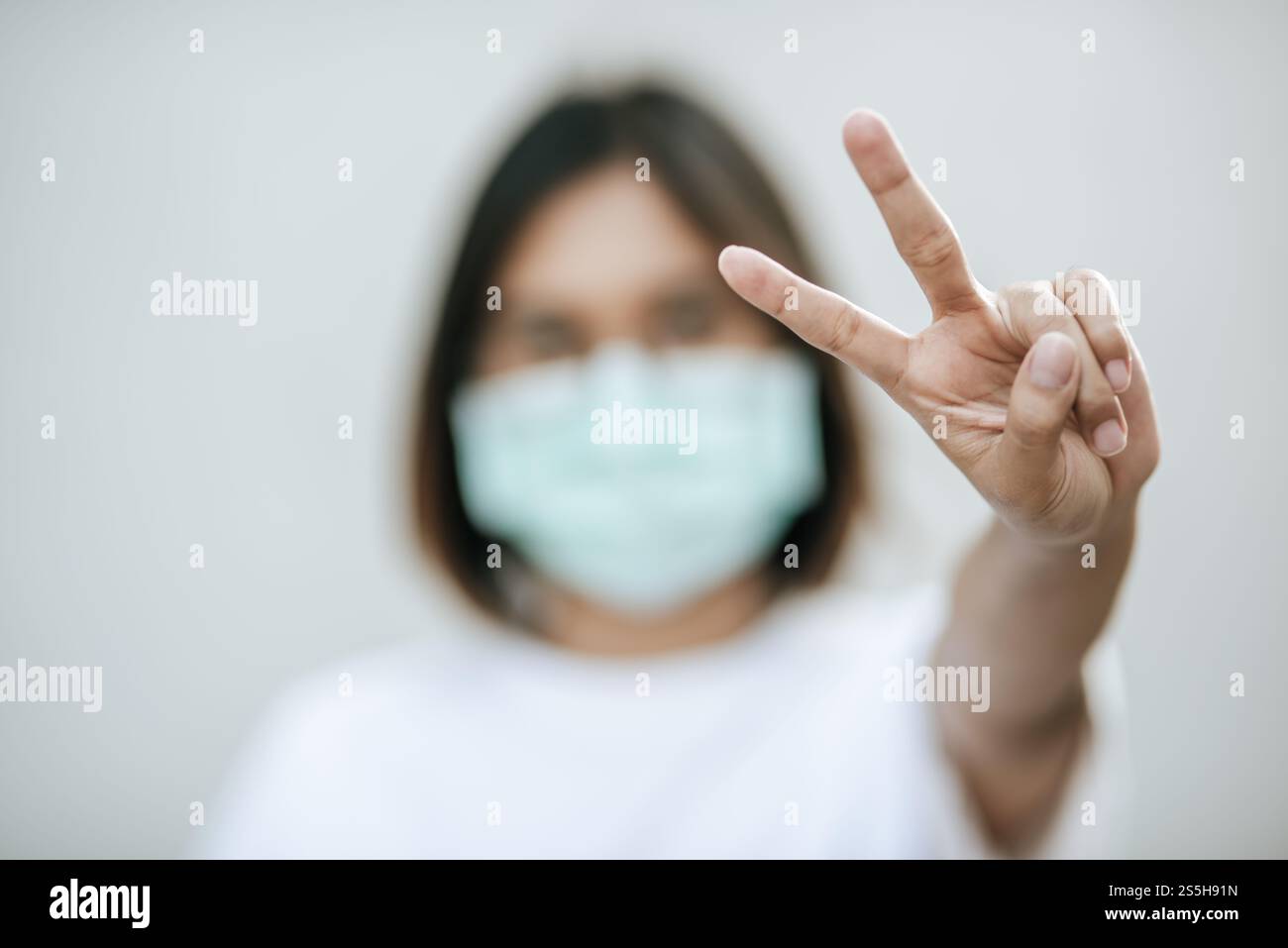 Donna che indossa una maschera e solleva due dita. Messa a fuoco selettiva. Foto Stock