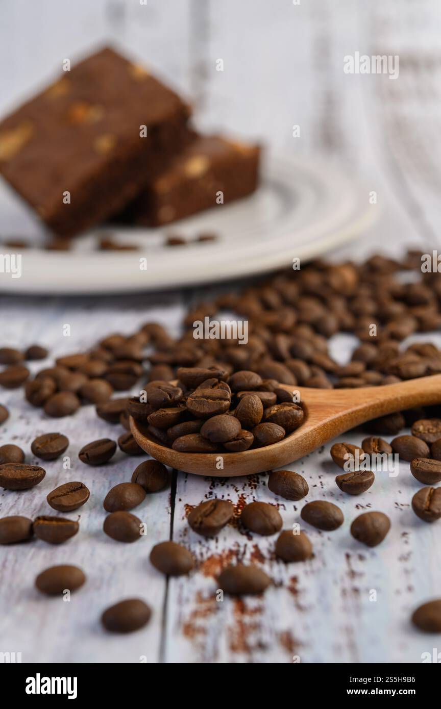 Chicchi di caffè su cucchiaio di legno e brownie al cioccolato su un tavolo di legno bianco. Foto Stock