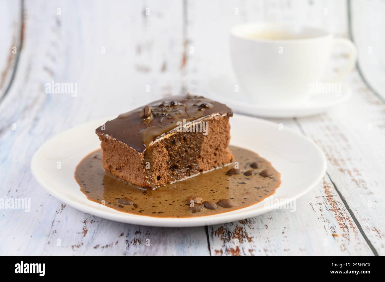 Torta al cioccolato ricoperta di caffè su un piatto bianco con chicchi di caffè su un tavolo di legno. Foto Stock