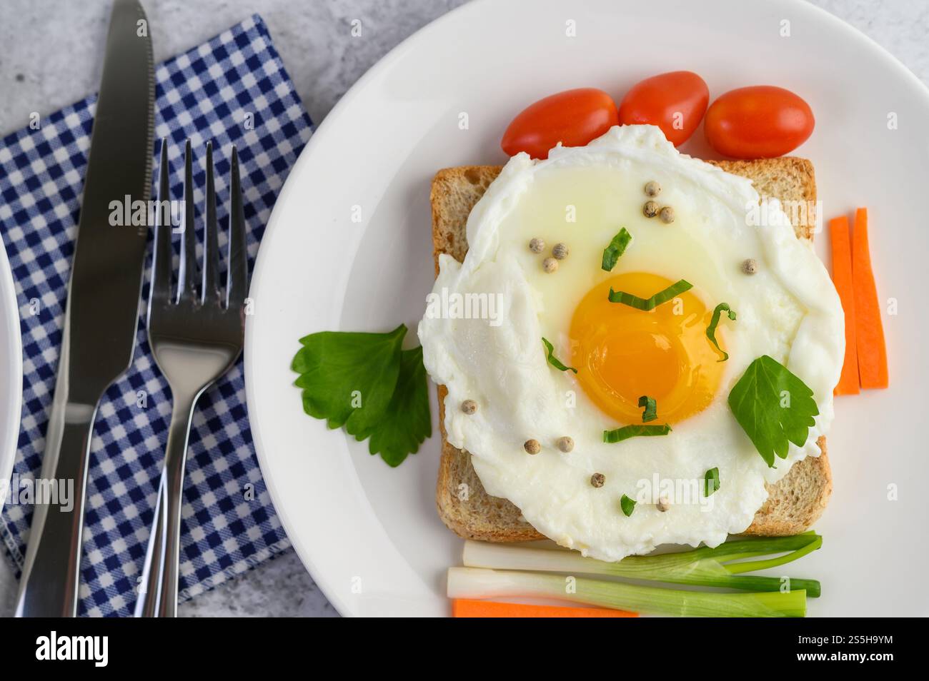Un uovo fritto adagiato su un toast, ricoperto di semi di pepe con carote e cipollotti. Foto Stock
