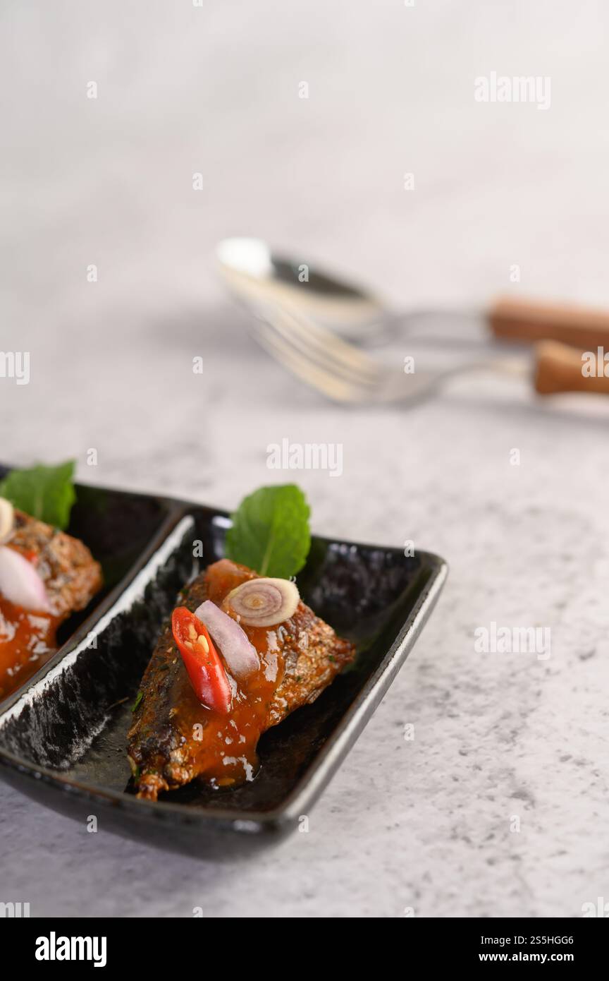 Stuzzichini selettivi con la sardina piccante in vassoio di ceramica, cucchiaio e forchetta su sfondo sfocato, spazio per copiare Foto Stock