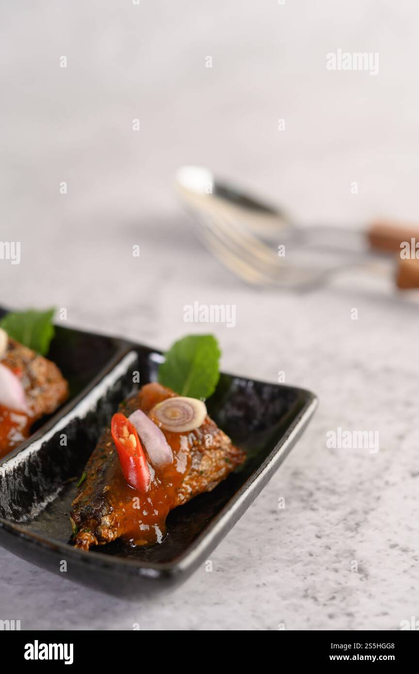 Stuzzichini selettivi con la sardina piccante in vassoio di ceramica, cucchiaio e forchetta su sfondo sfocato, spazio per copiare Foto Stock