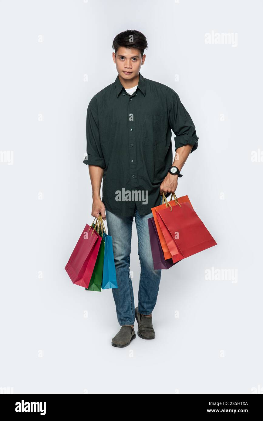 Un giovane che indossa una camicia nera e un jeans porta molte borse per andare a fare shopping. Foto Stock