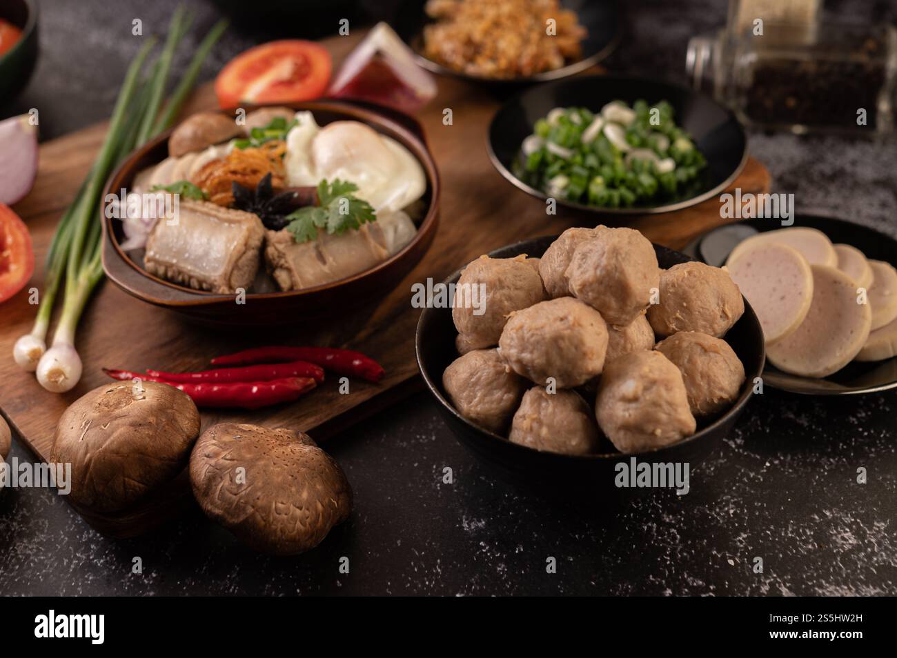 Polpette di maiale in tazze nere con cipolla primaverile, peperoncino, funghi shiitake e pomodoro. Foto Stock