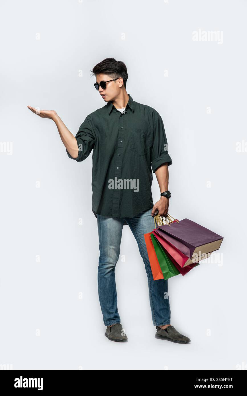 Un giovane che indossa una camicia nera e un jeans porta molte borse per andare a fare shopping. Foto Stock