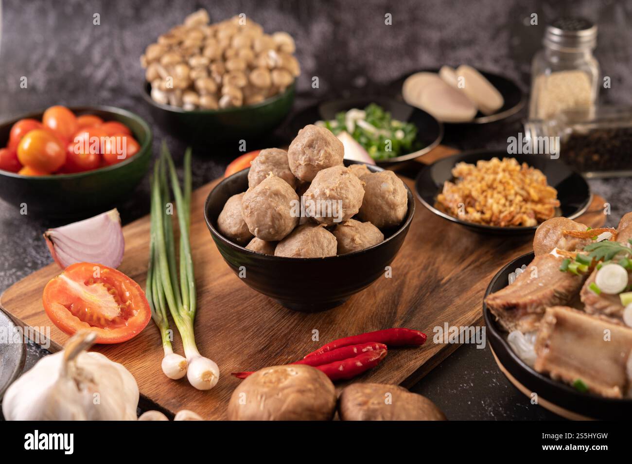 Polpette di maiale in tazze nere con cipolla primaverile, peperoncino, funghi shiitake e pomodoro. Foto Stock
