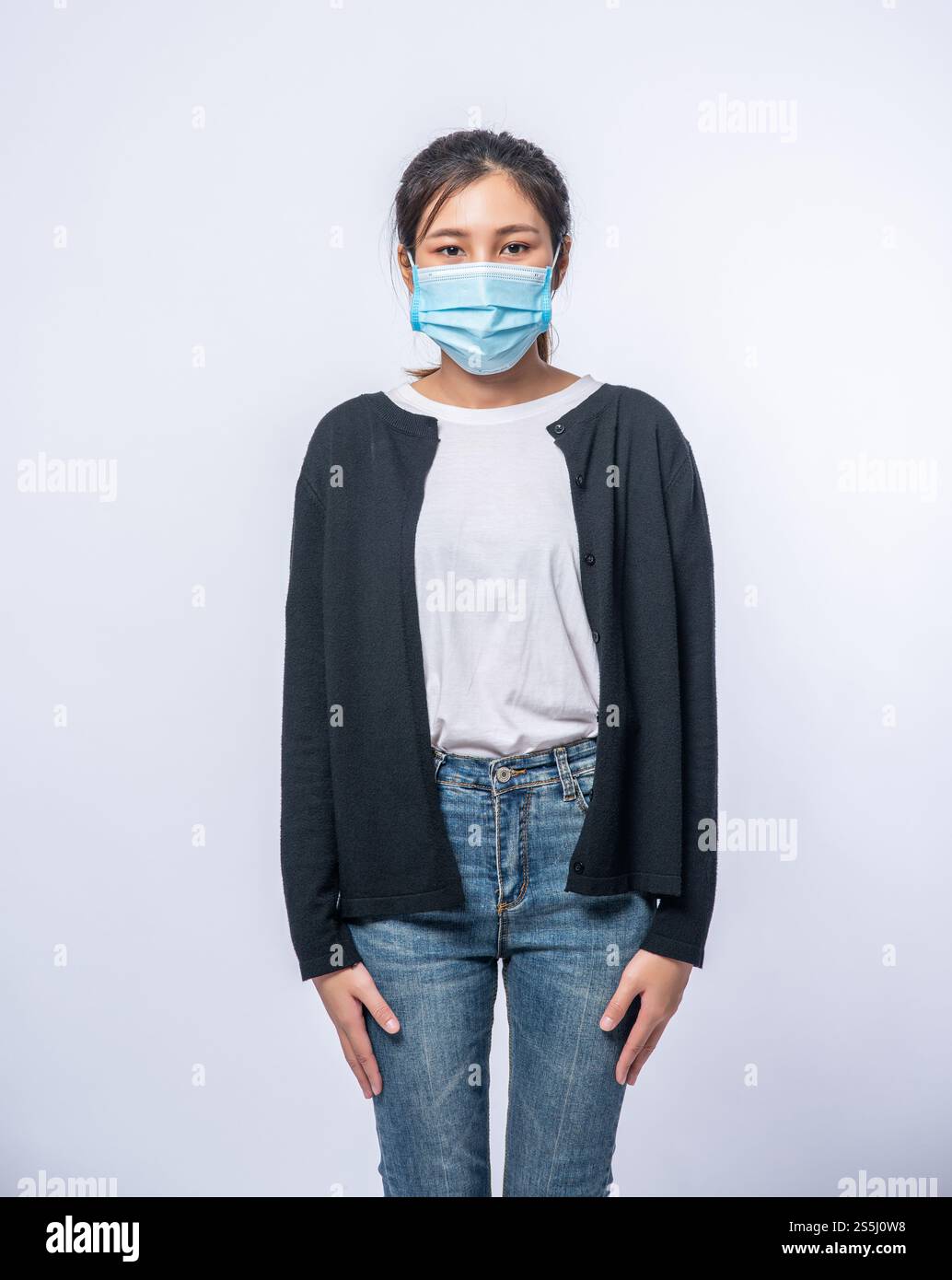 Una donna è malata in piedi e indossa una maschera. Indossa un cappotto nero e un paio di jeans. Foto Stock