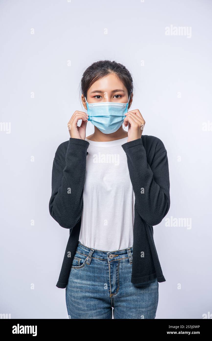 Una donna è malata in piedi e indossa una maschera. Indossa un cappotto nero e un paio di jeans. Foto Stock