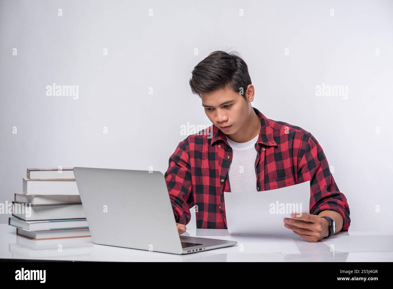 Un uomo che usa un portatile in ufficio e fa un'analisi documentale. Foto Stock