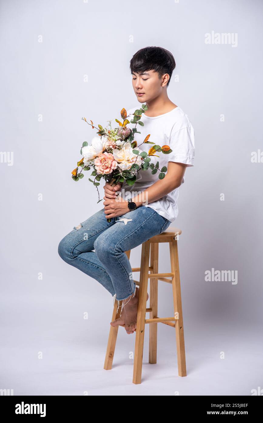 Un giovane con una t-shirt bianca si siede su un seggiolone e tiene i fiori. Foto Stock