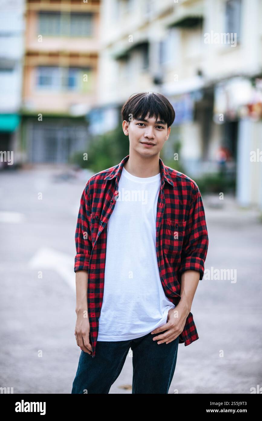 Un giovane uomo con una camicia a righe è in piedi per strada. Foto Stock