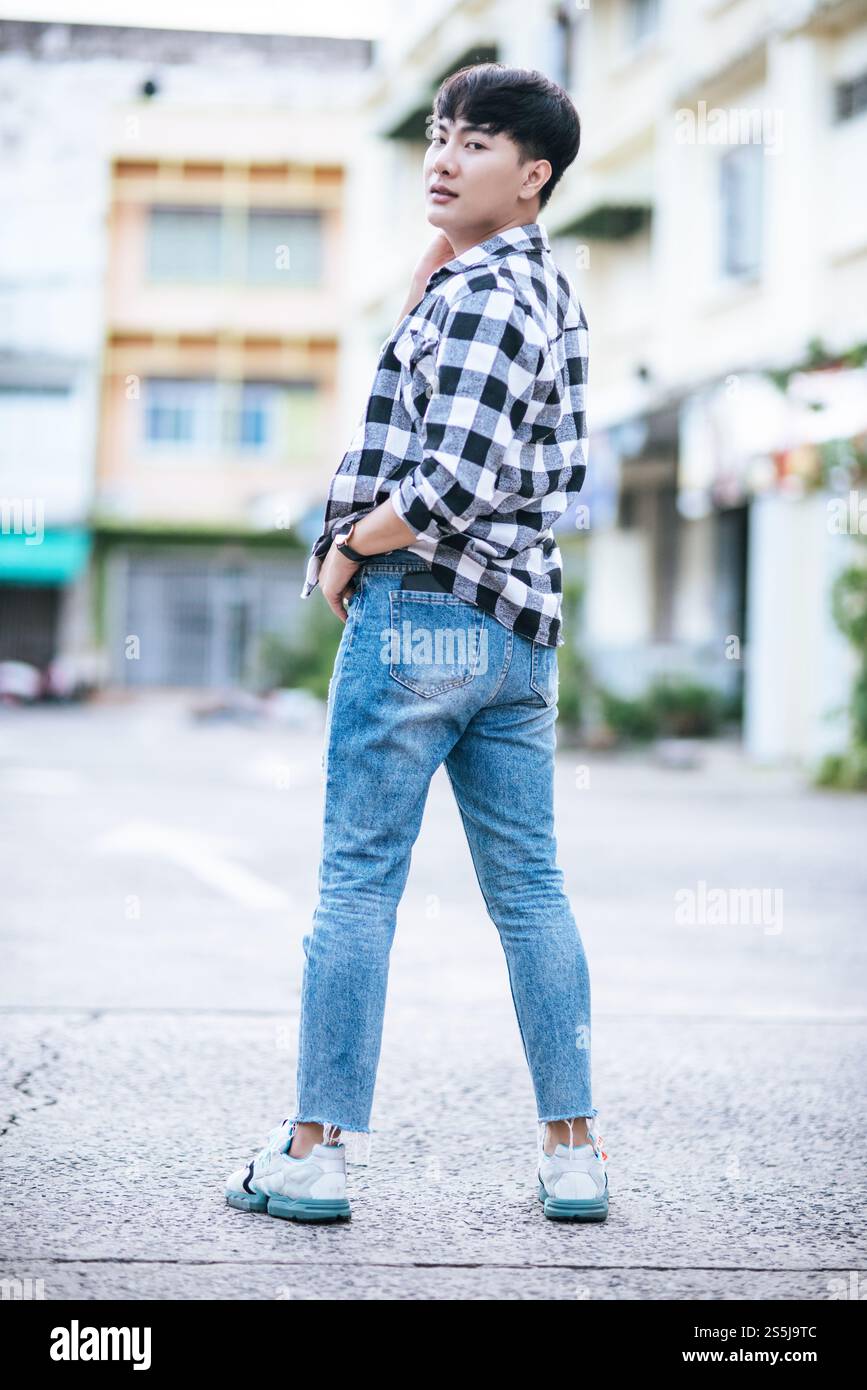 Un giovane uomo con una camicia a righe è in piedi per strada. Foto Stock