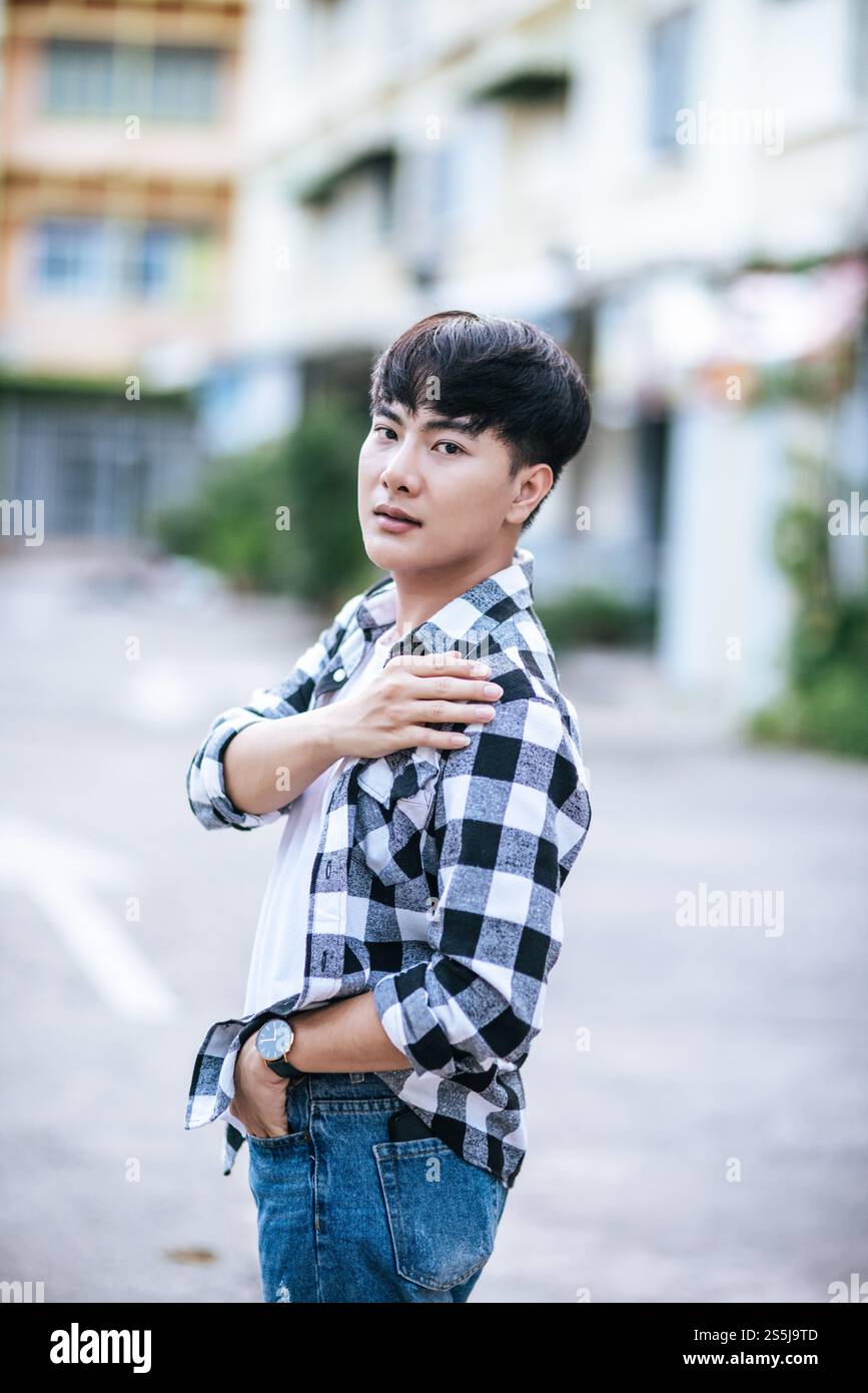 Un giovane uomo con una camicia a righe è in piedi per strada. Foto Stock