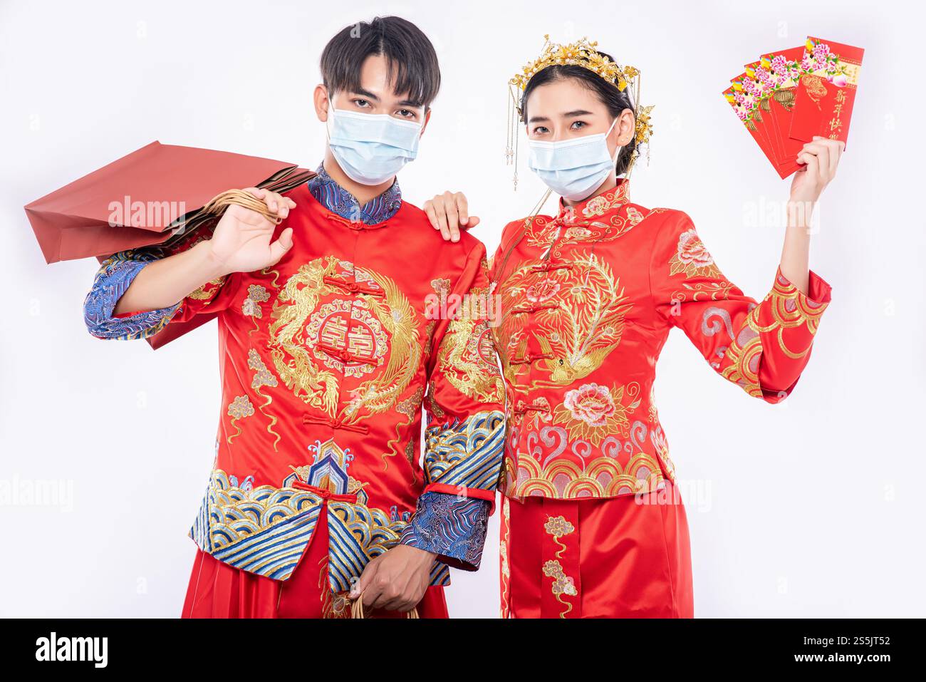 Uomini e donne che indossano Qipao e che indossano maschere che trasportano sacchetti di carta per fare acquisti con busta rossa Foto Stock