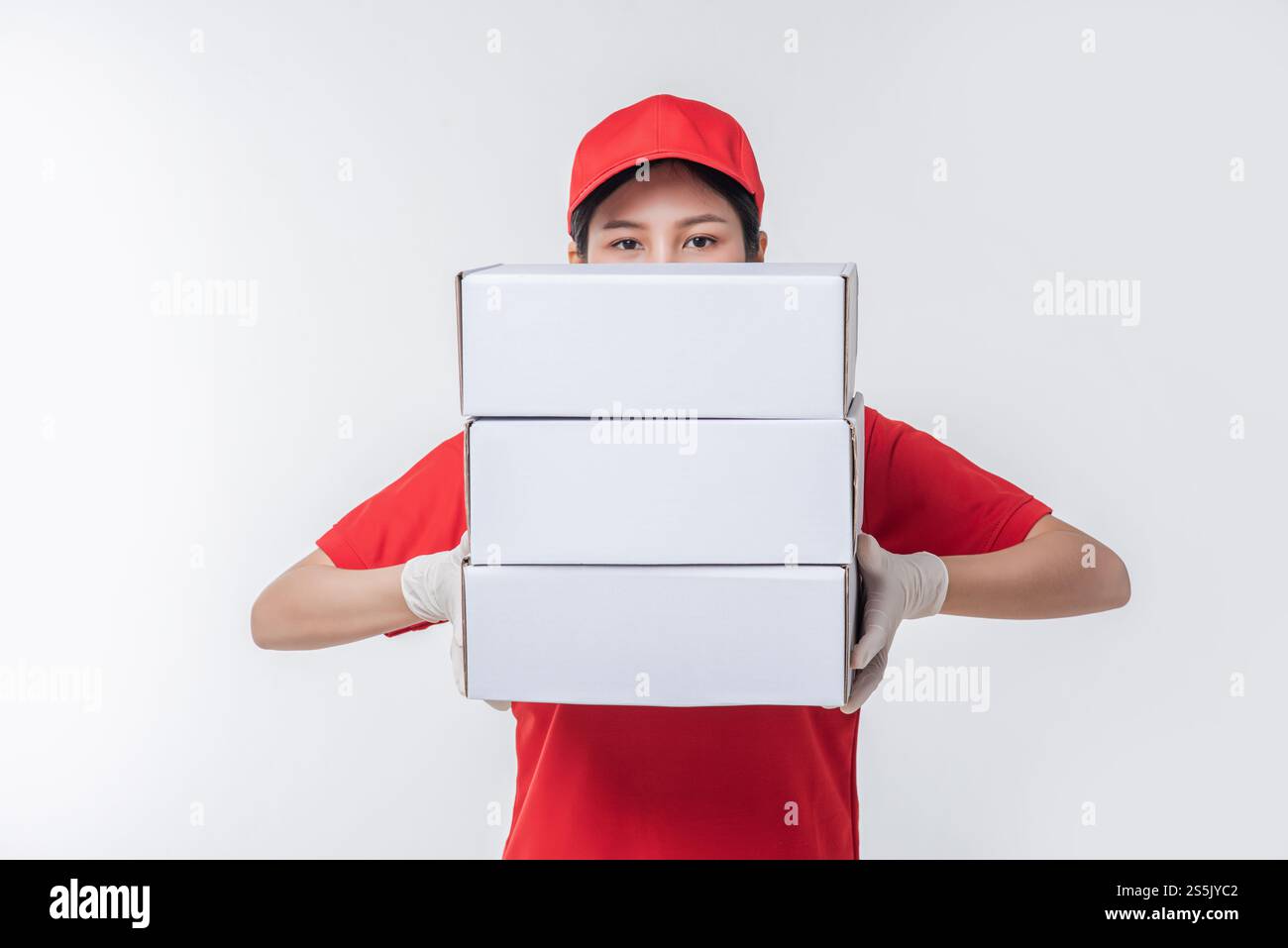 Immagine di un giovane fattorino in maglietta bianca con cappuccio rosso in piedi con scatola di cartone bianca vuota isolata su sfondo grigio chiaro studio Foto Stock
