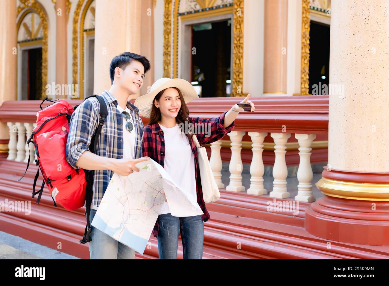 Giovane coppia asiatica di backpacker in un bellissimo tempio durante le vacanze in Thailandia, bella donna indossa il sombrero che indica dove vogliono andare, tengono Foto Stock