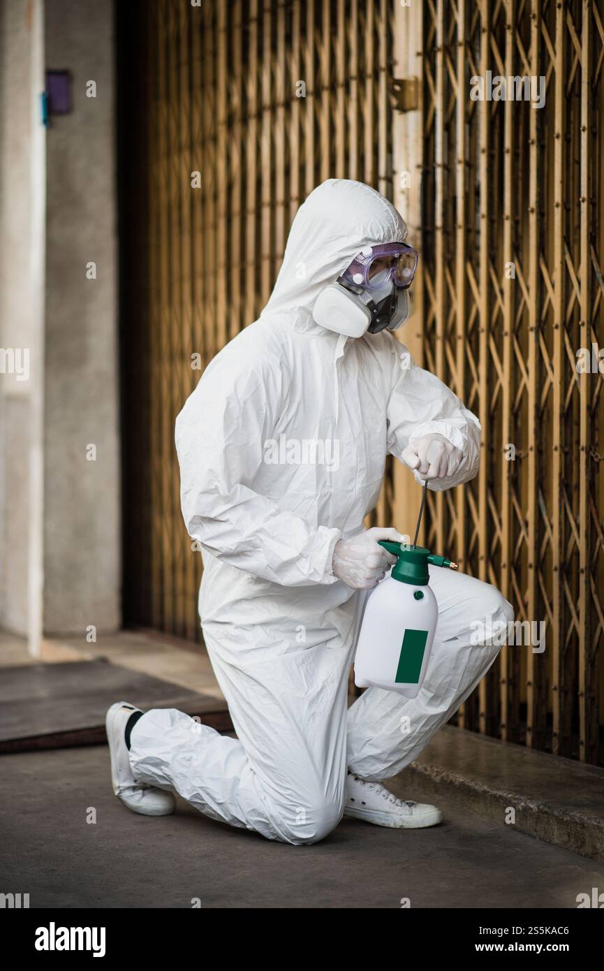 Specialista di disinfezione uomo che indossa i dispositivi di protezione individuale (dpi) tuta, guanti, maschera e occhiali trasparenti, pulizia strade con bottiglia di Foto Stock