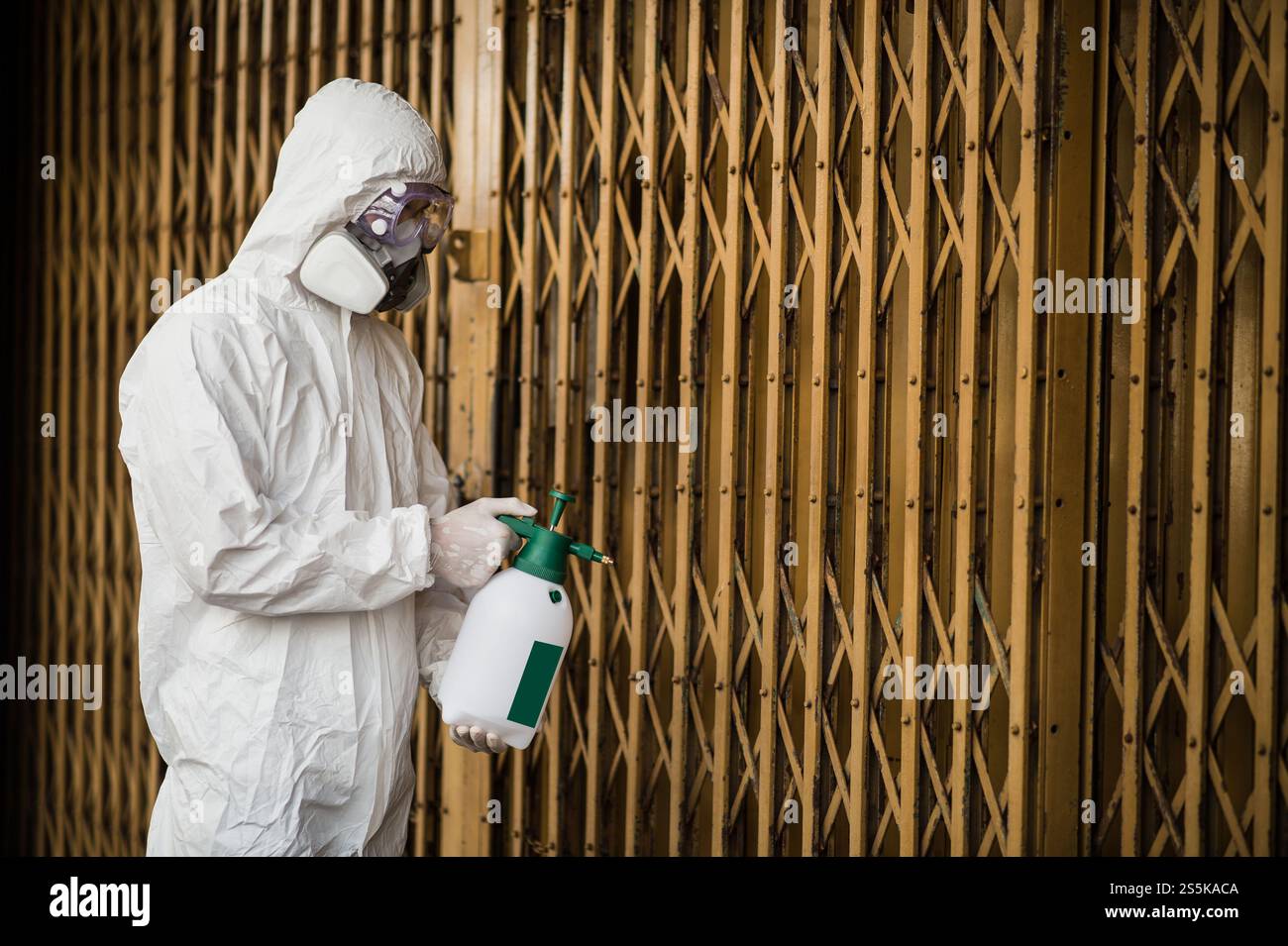 Specialista di disinfezione uomo che indossa i dispositivi di protezione individuale (dpi) tuta, guanti, maschera e occhiali trasparenti, pulizia strade con bottiglia di Foto Stock