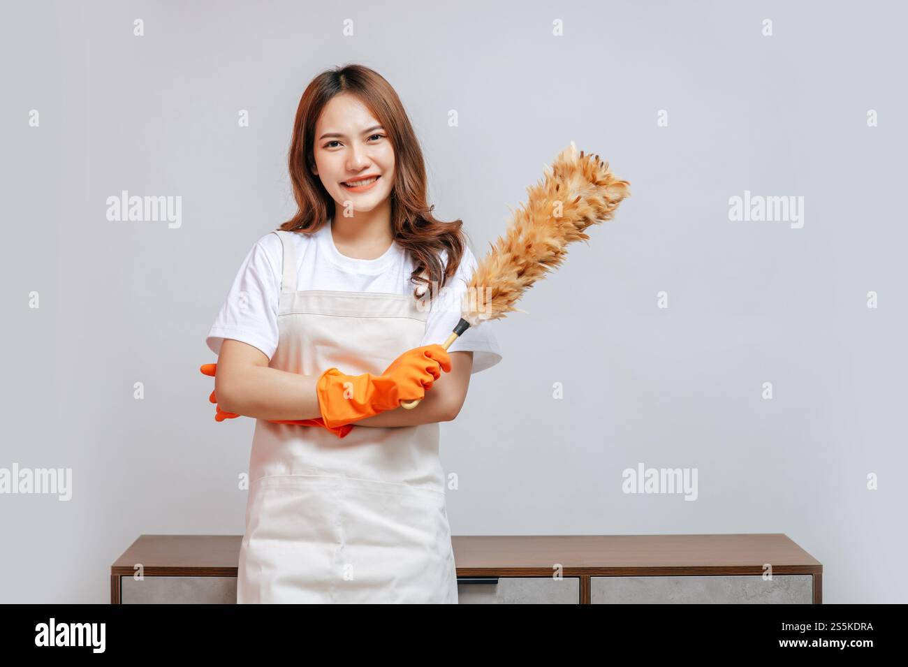 Ritratti la giovane bella donna felice con grembiule e guanti di gomma che reggono una spugna di piume preparandosi a pulire, sorridere e guardare alla macchina fotografica, copiare spazio Foto Stock