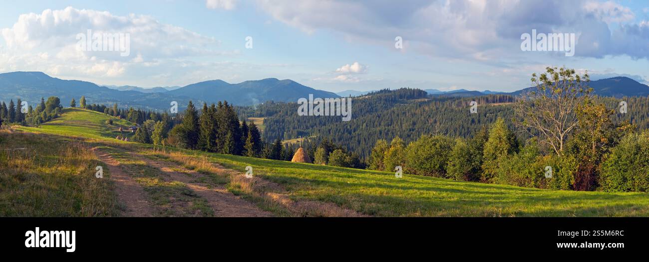 Vista panoramica serata montagna con strada terra, haystackes e tenuta di campagna (periferia villaggio Slavske, MTS Carpazi, Ucraina). Foto Stock