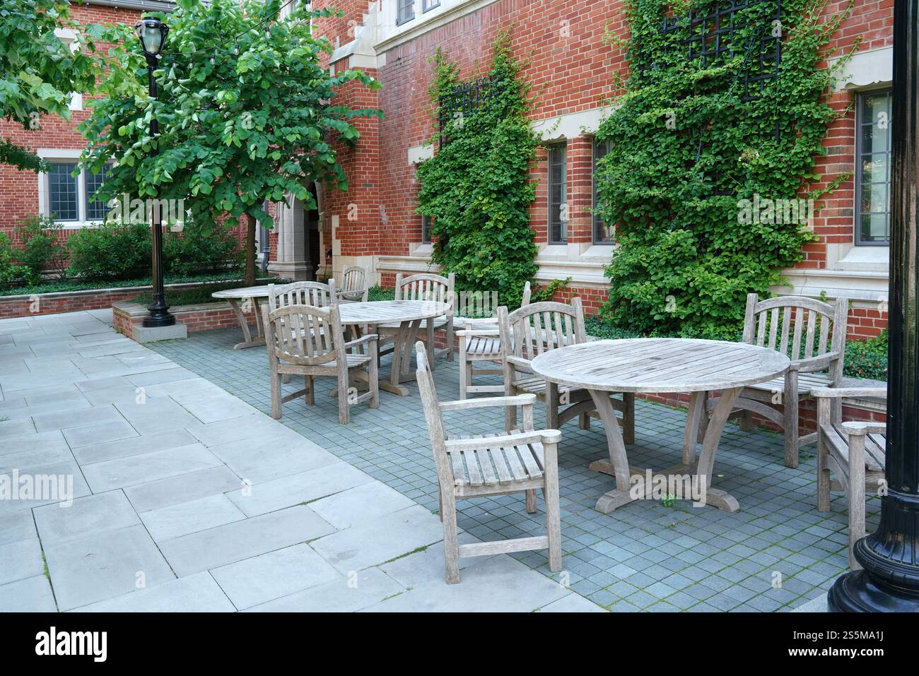 Tavoli e sedie in legno su un patio accanto ad un edificio in mattoni ricoperti di edera Foto Stock