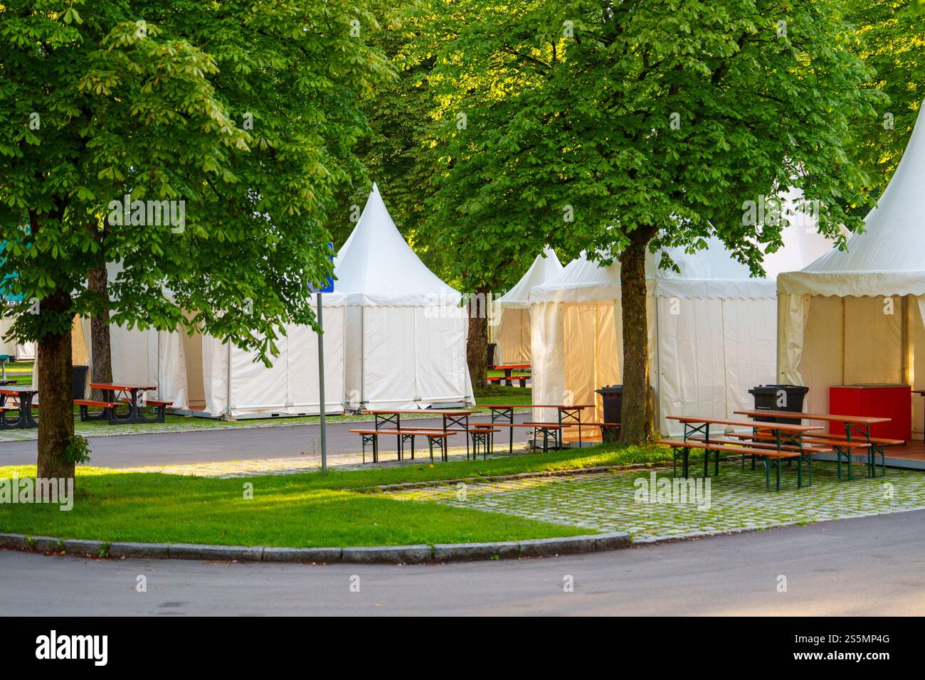 Una fila di eleganti tende White Party allestite in uno splendido parco circondato da lussureggianti alberi verdi. Foto Stock