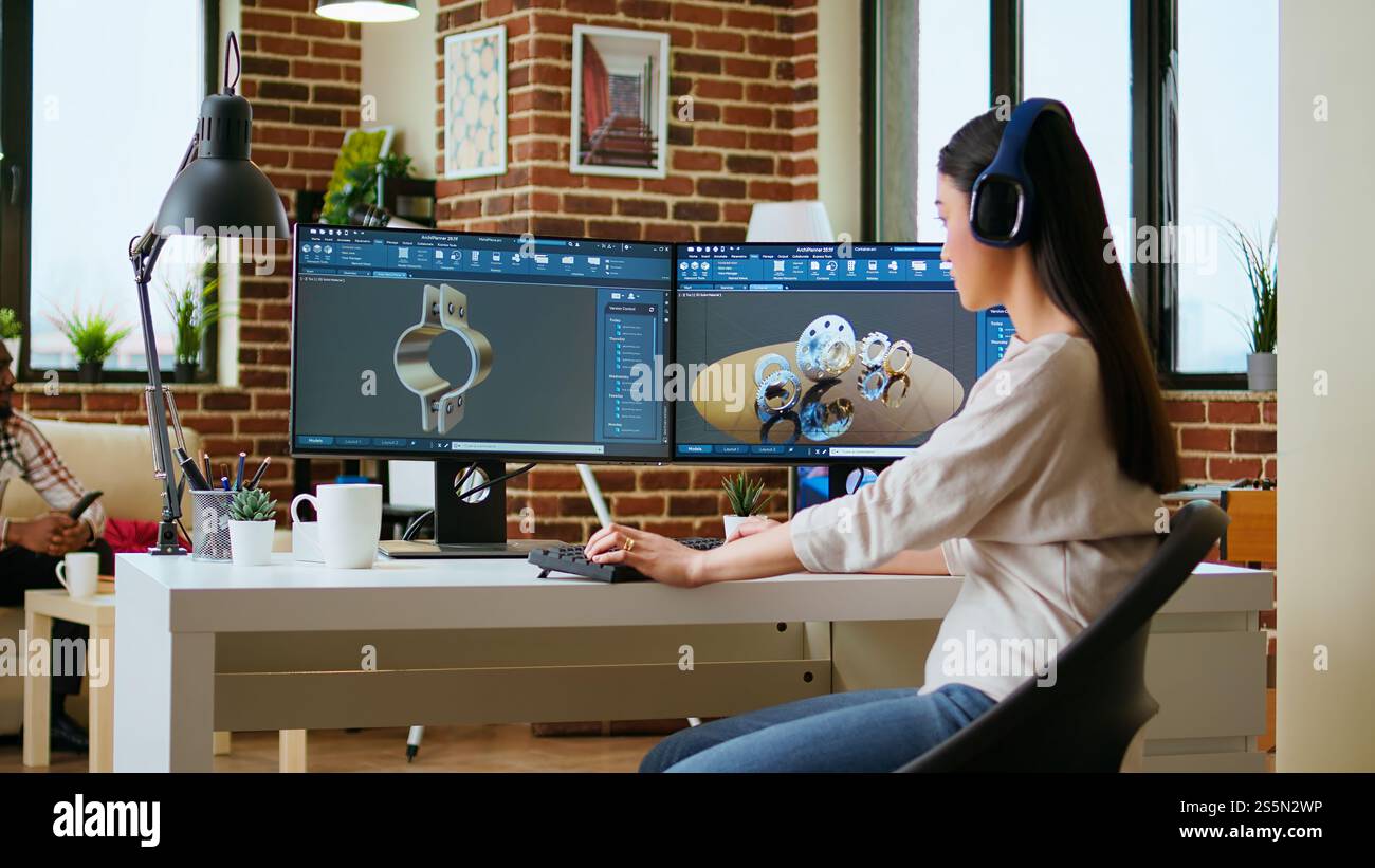 L'ingegnere professionista asiatico lavora sulla codifica di progetti industriali utilizzando strumenti software avanzati. Il soggiorno e l'ufficio sono dotati di due monitor e di apparecchiature tecniche per una produttività elevata. Telecamera A.. Foto Stock