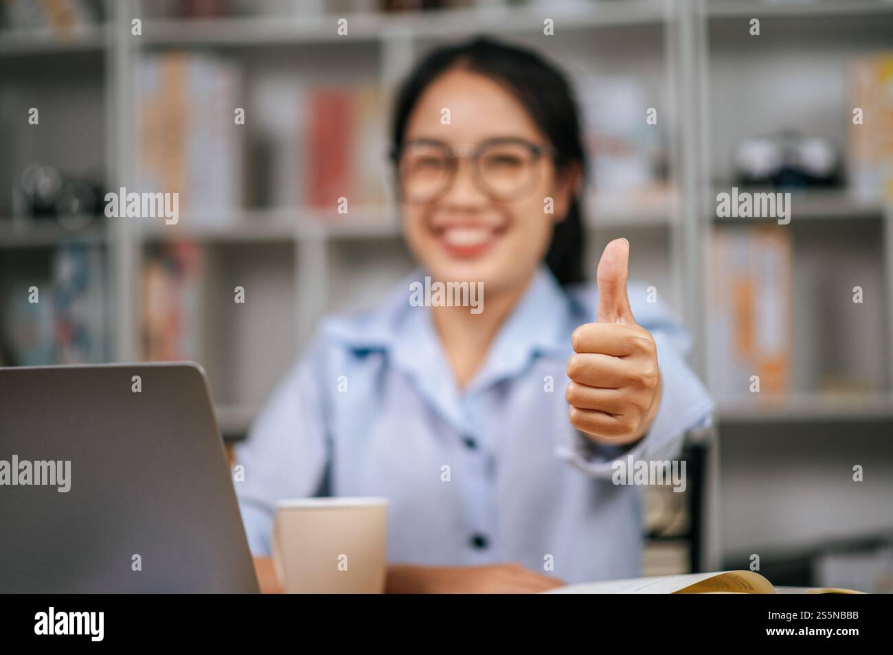 Primo piano e attenzione selettiva a portata di mano di una giovane donna seduta dietro un computer portatile alza la mano con un pizzico di buono e sorriso Foto Stock