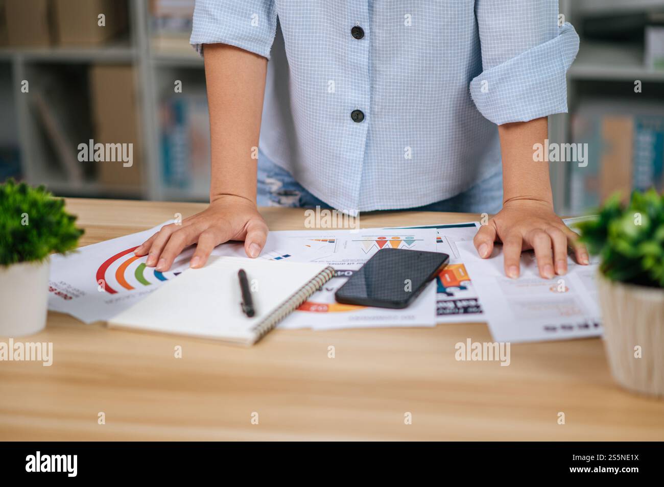 Primo piano e mano selettiva di una giovane donna con smartphone e notebook, documenti sulla scrivania in ufficio a casa, durante la quarantena covid-19 Foto Stock