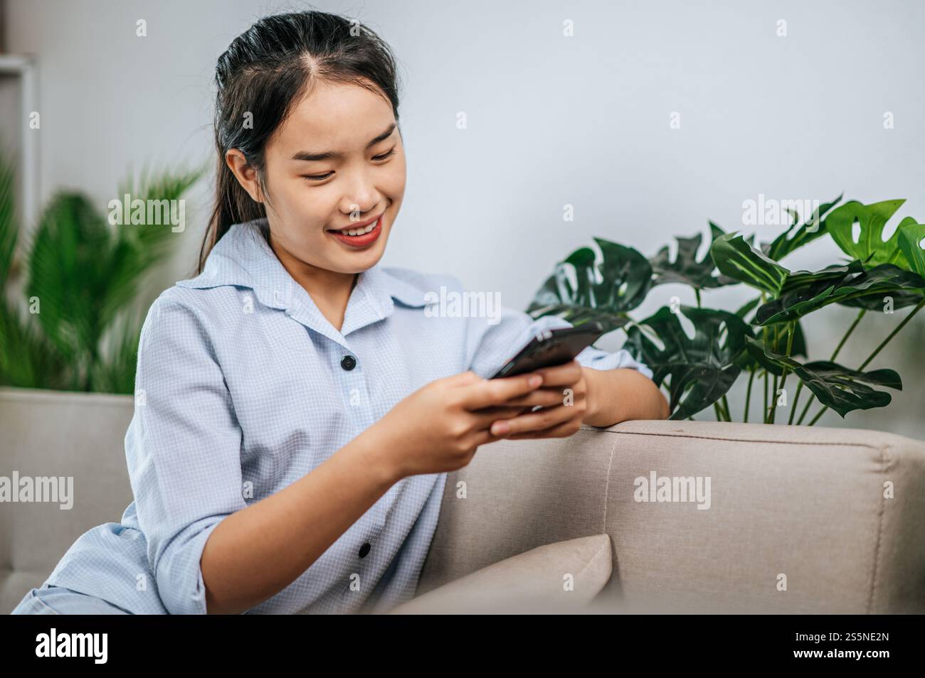 Smiley bella adolescente seduto sul divano e utilizzare lo smartphone per videochiamare o selfie, durante la quarantena covid-19 auto isolamento a casa Foto Stock