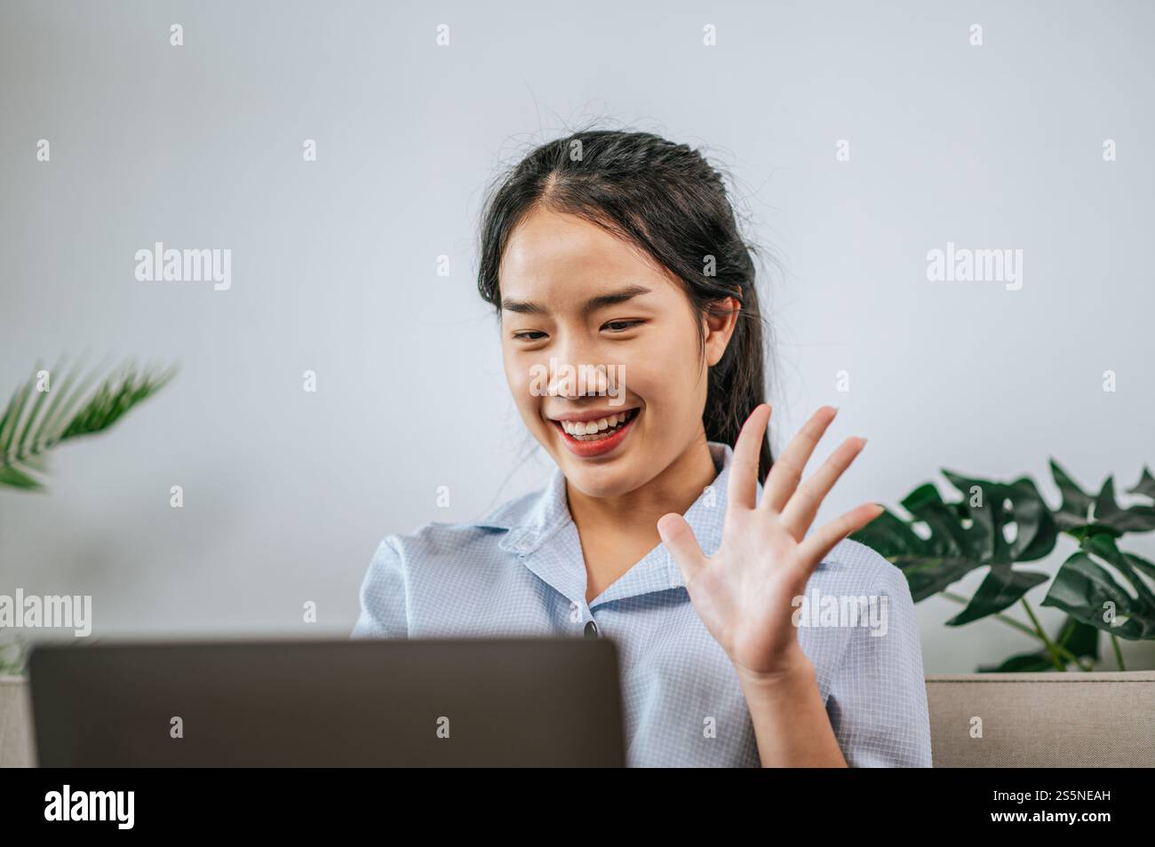 La giovane donna asiatica usa il computer portatile per videochiamare in salotto a casa Foto Stock