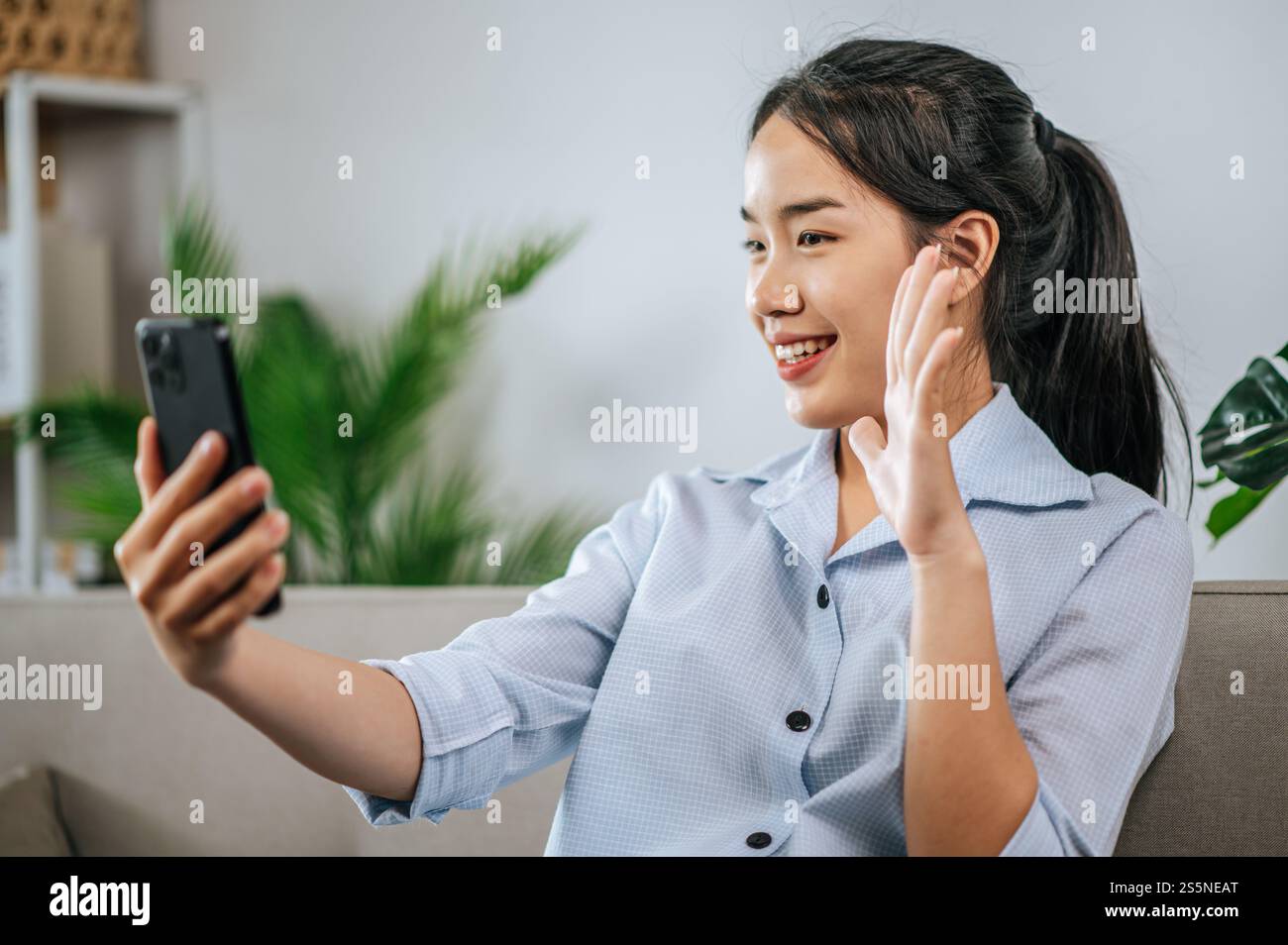 Smiley bella adolescente seduto sul divano e utilizzare lo smartphone per videochiamare o selfie, durante la quarantena covid-19 auto isolamento a casa Foto Stock