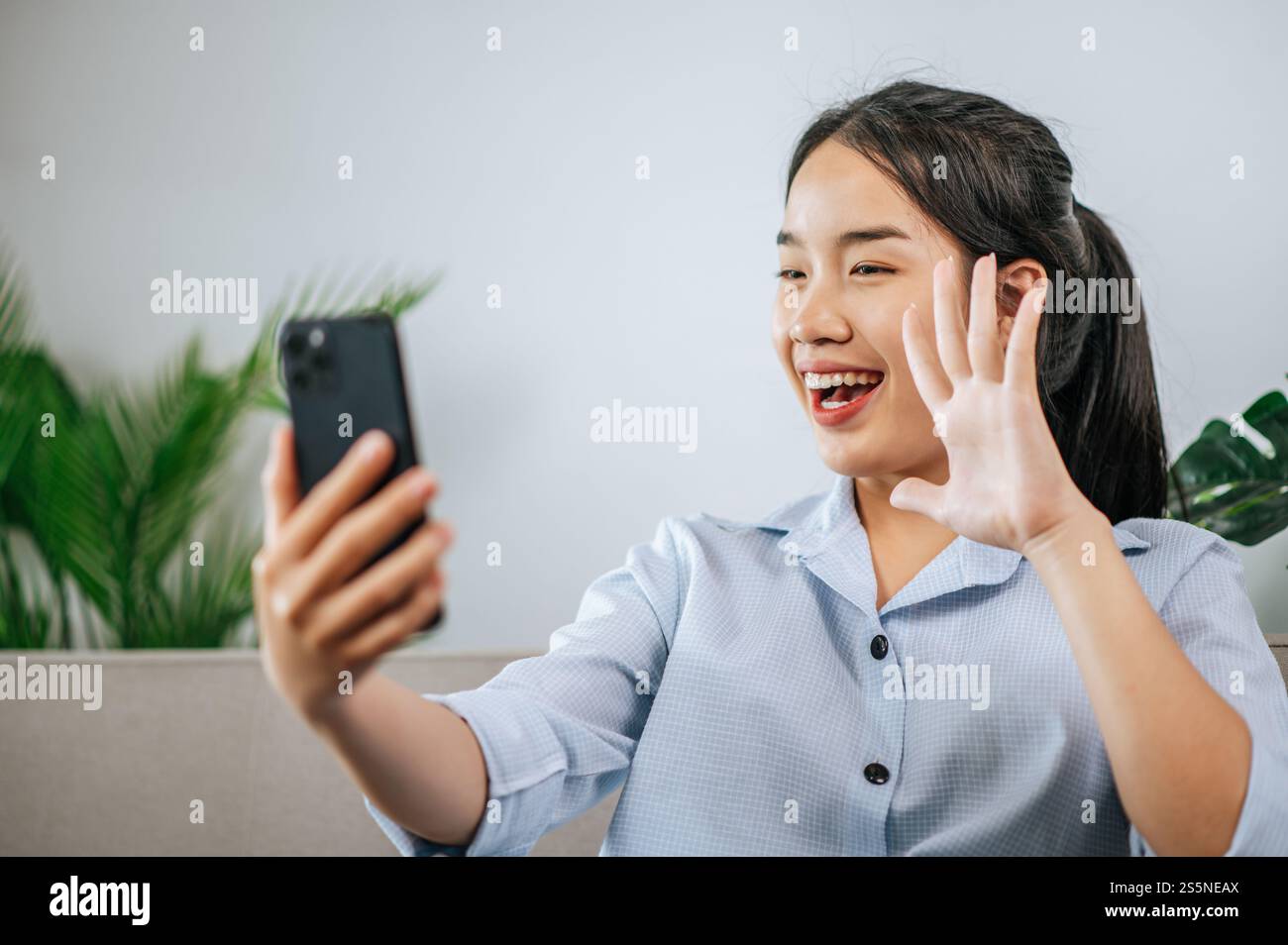 Smiley bella adolescente seduto sul divano e utilizzare lo smartphone per videochiamare o selfie, durante la quarantena covid-19 auto isolamento a casa Foto Stock