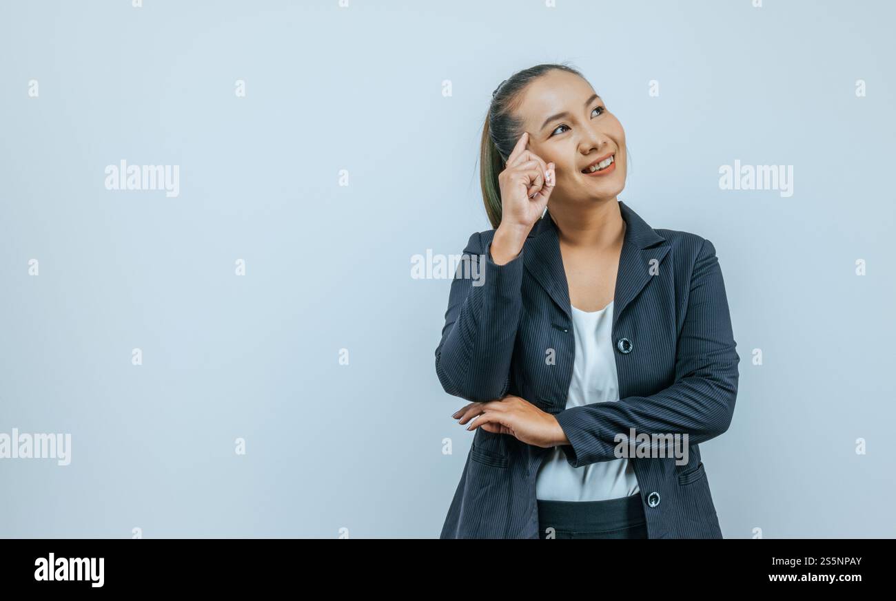 Ritratto di donna asiatica sorridente che indossa abiti casual che puntano alla testa con un dito e guardano lontano lo spazio vuoto a parte, isolato sopra Foto Stock