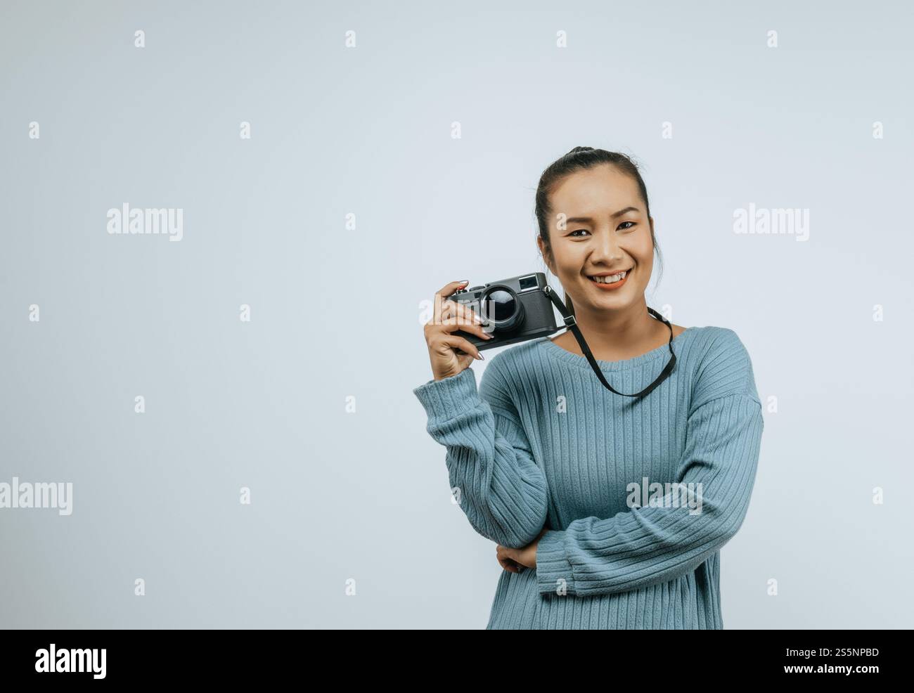 Ritratto di donna asiatica che indossa abiti casual con un grande sorriso sul viso, tenendo in mano una macchina fotografica per scattare una foto. Sfondo isolato in studio con vuoto Foto Stock