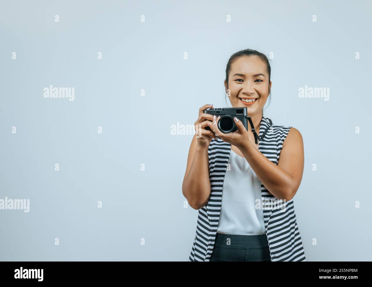 Ritratto di donna asiatica che indossa abiti casual con un grande sorriso sul viso, tenendo in mano una macchina fotografica per scattare una foto. Sfondo isolato in studio con vuoto Foto Stock