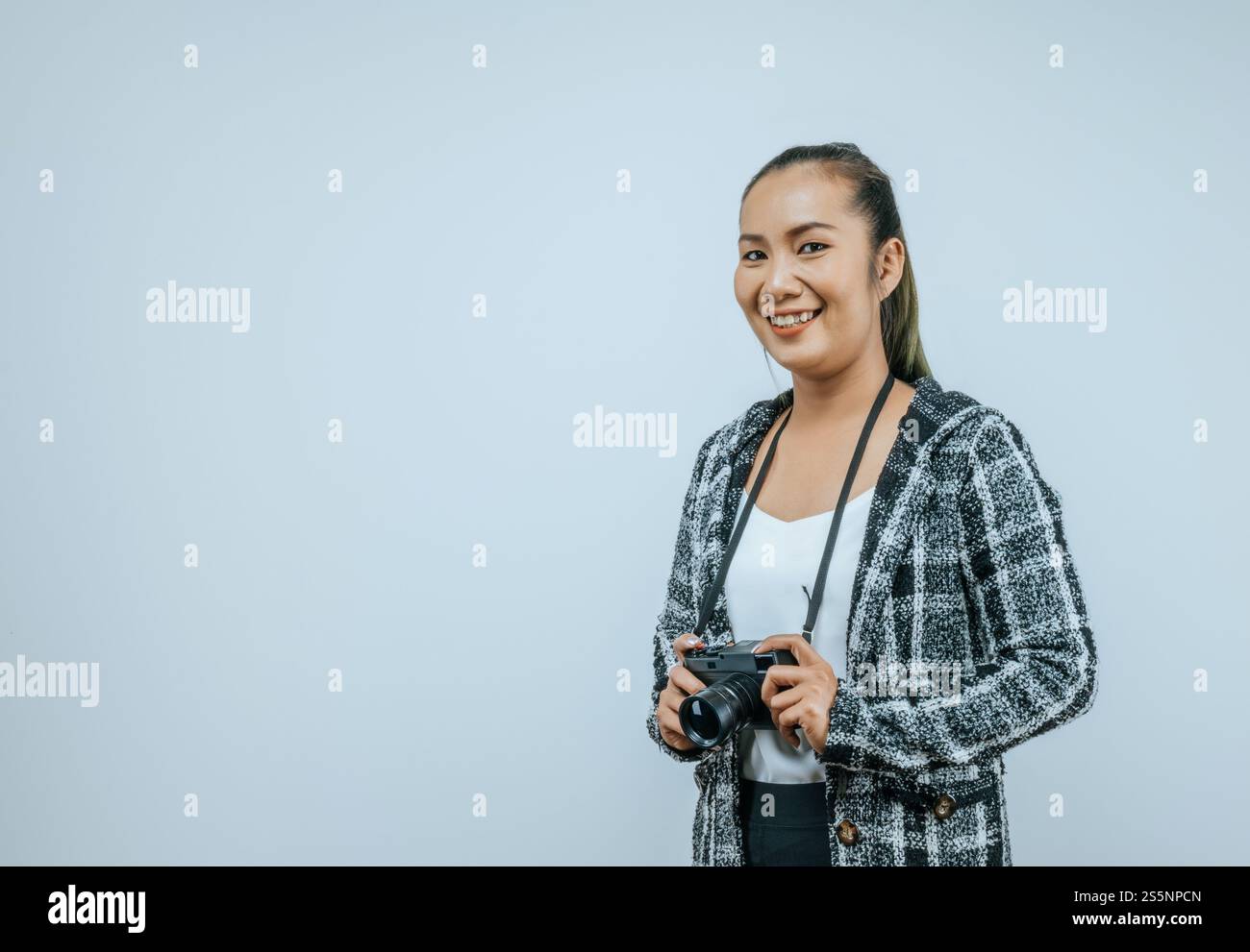 Ritratto di donna asiatica che indossa abiti casual con un grande sorriso sul viso, tenendo in mano una macchina fotografica per scattare una foto. Sfondo isolato in studio con vuoto Foto Stock
