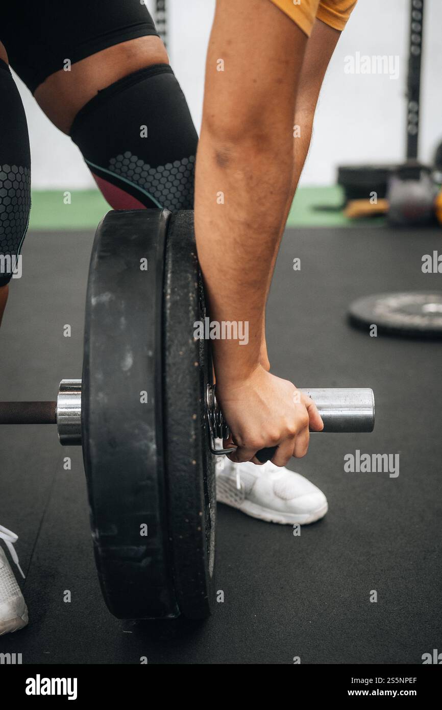 Primo piano della mano di un atleta che regola i piatti del barbell durante un allenamento in palestra, mostrando forza, concentrazione e attenzione ai dettagli nel sollevamento pesi Foto Stock