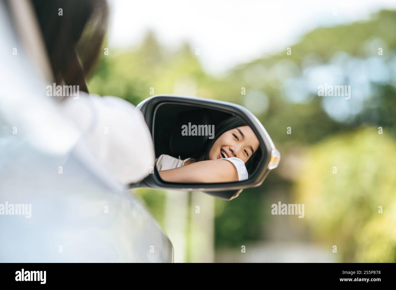 Una donna che guida un'auto sorride felicemente e guarda nello specchio laterale. Foto Stock