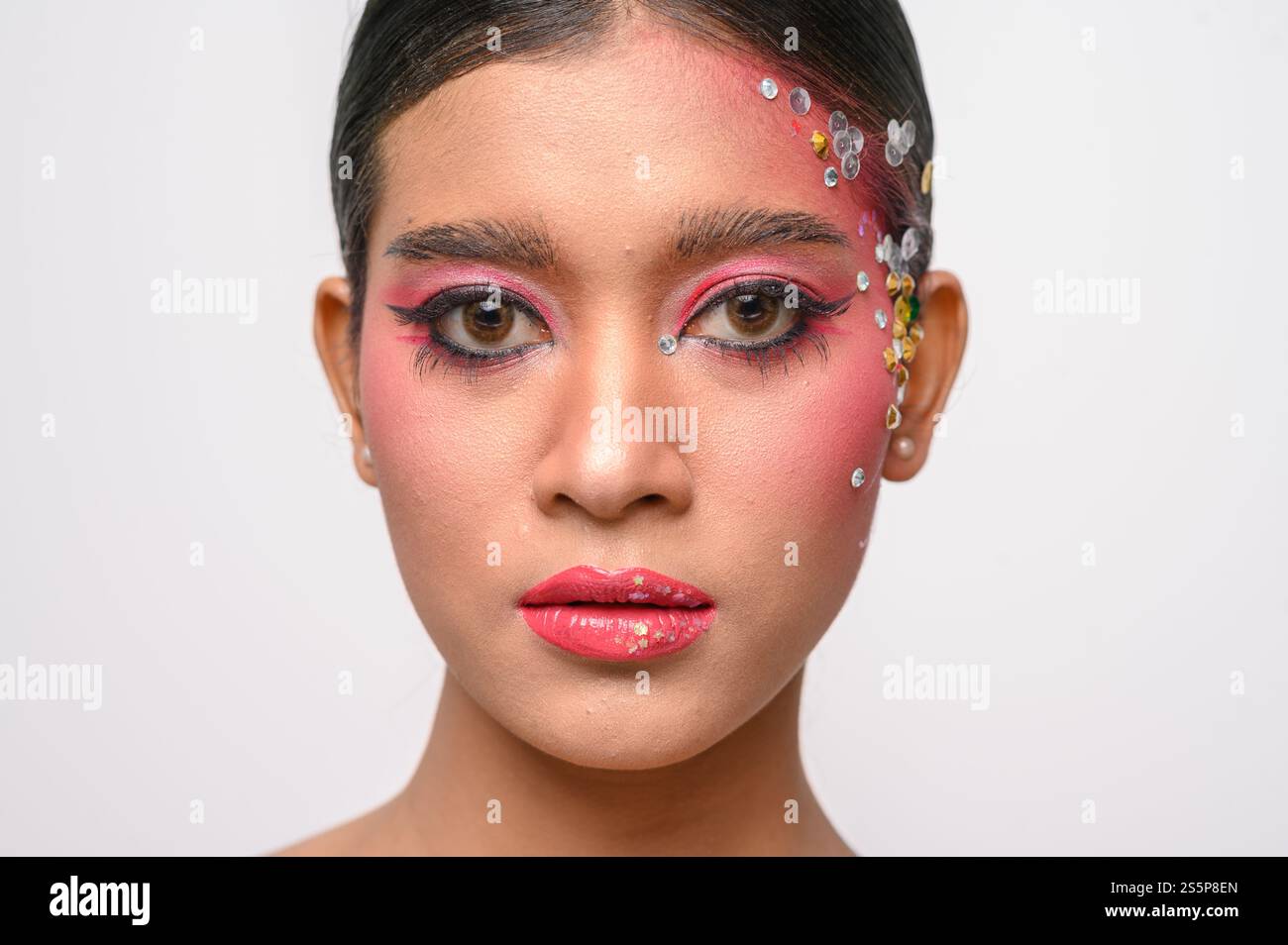 Donna che indossa trucco e decorazioni rosa sul viso. Isolato su sfondo bianco Foto Stock