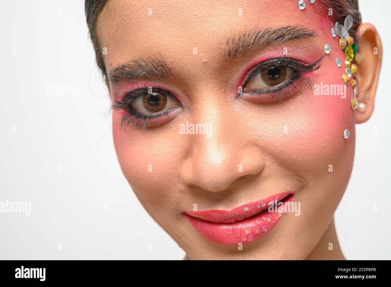 Donna che indossa trucco e decorazioni rosa sul viso. Isolato su sfondo bianco Foto Stock