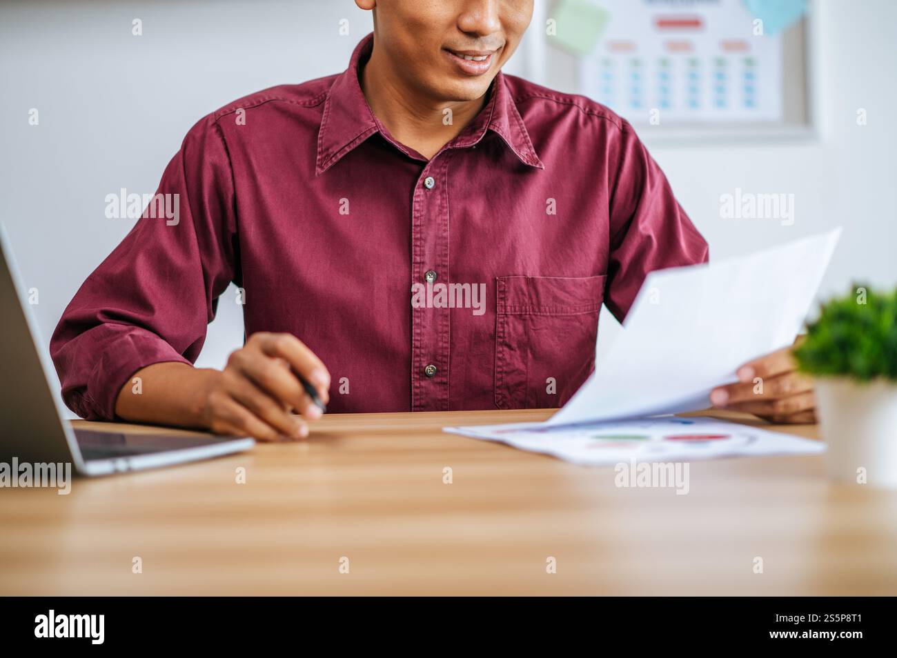 Un uomo che lavora in ufficio con un portatile, documenti sulla scrivania. Foto Stock