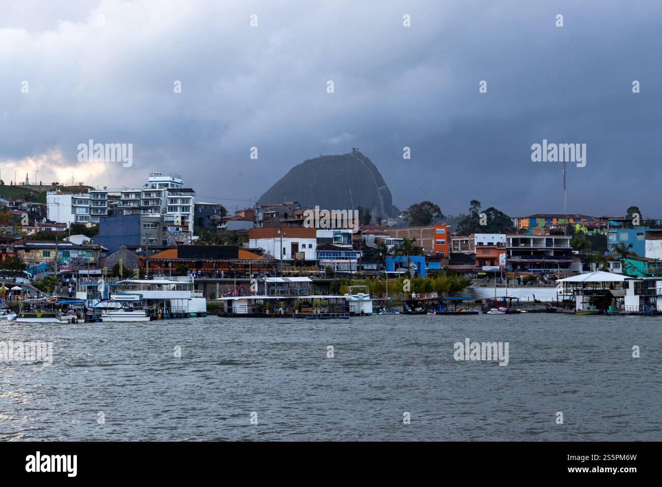 Una vista panoramica di una città colorata sul lungomare, con un'iconica grande formazione rocciosa sullo sfondo sotto cieli nuvolosi, catturando la città Foto Stock