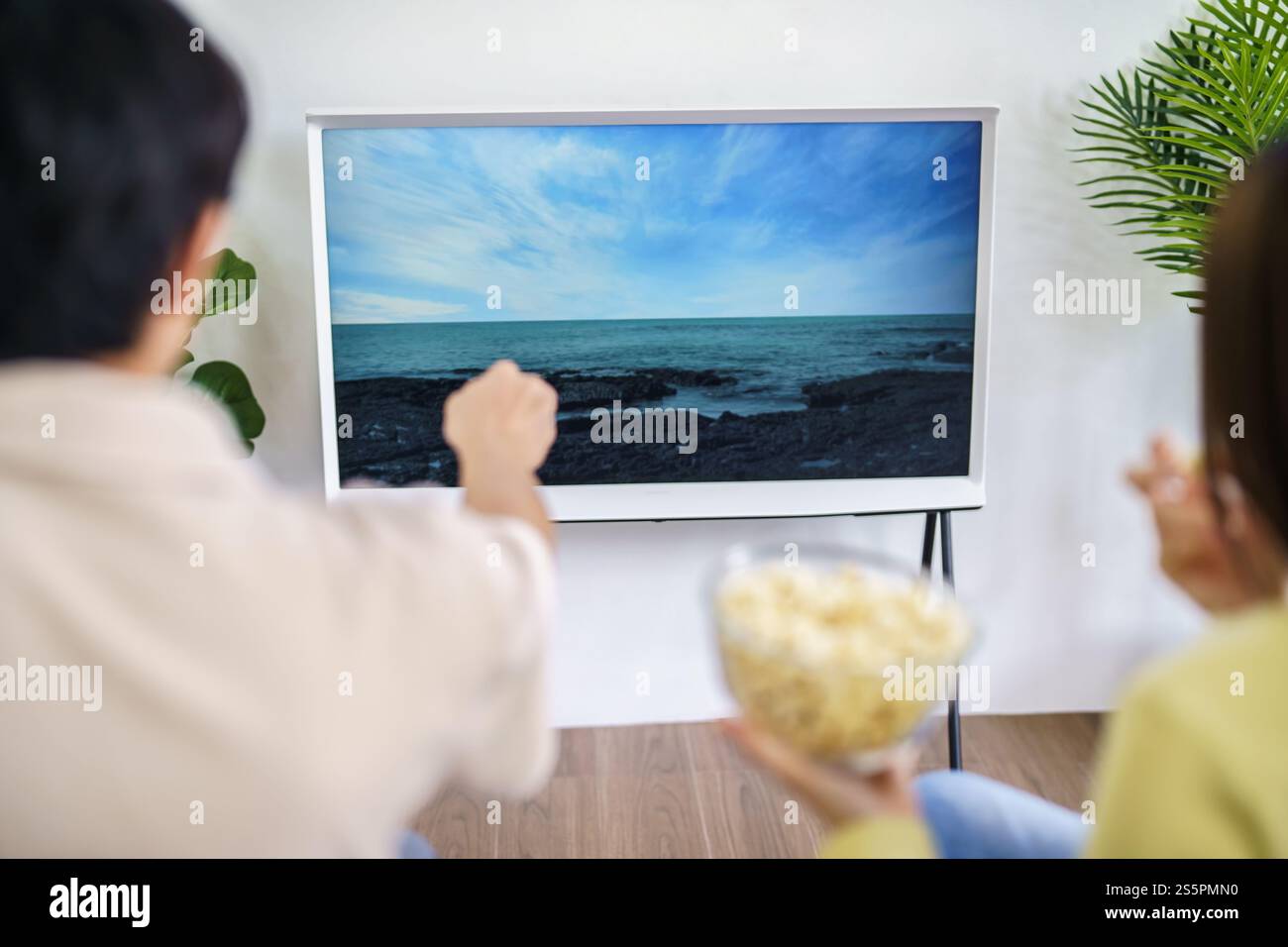 Famiglia asiatica che guarda la smart TV insieme e usa il telecomando che tiene i popcorn a casa con il telecomando per guardare film o serie TV Foto Stock