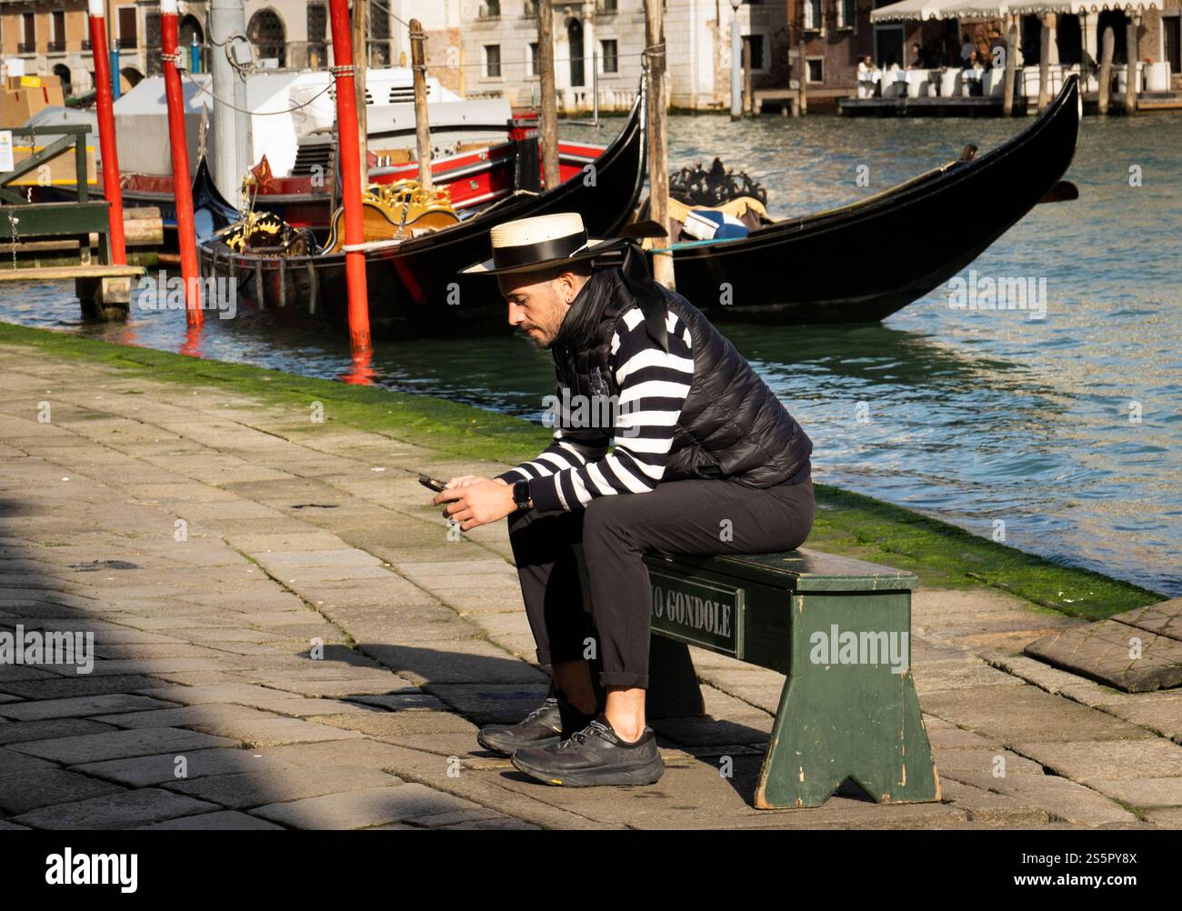 Un gondoliere si siede con il suo telefono vicino a un canale a Venezia, in Italia. Foto Stock